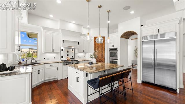 13625 Random Ridge View Colorado Springs, CO 80921 - Photo 10 of 50 Kitchen featuring light stone countertops, stainless steel appliances, white cabinets, dark wood-style flooring, and recessed lighting