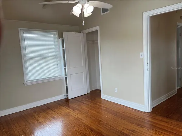 an empty room with wooden floor chandelier fan and windows