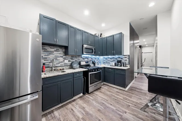 a kitchen with stainless steel appliances kitchen island granite countertop a refrigerator a sink dishwasher and a stove top oven with wooden floor