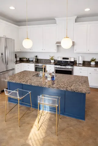 a kitchen with kitchen island granite countertop a sink a stove a counter space and cabinets