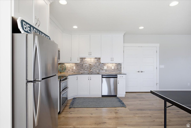 21 Pier Place Tooele, UT 84074 - Photo 55 of 112 Modern kitchen area featuring stainless steel appliances, white cabinetry, a mosaic tile backsplash, and light wood-finish flooring