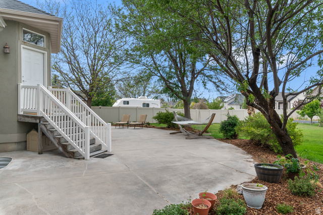 439 East 13540 South Draper, UT 84020 - Photo 37 of 46 Expansive concrete patio with white railing stairs leading to a side door, framed by mature trees