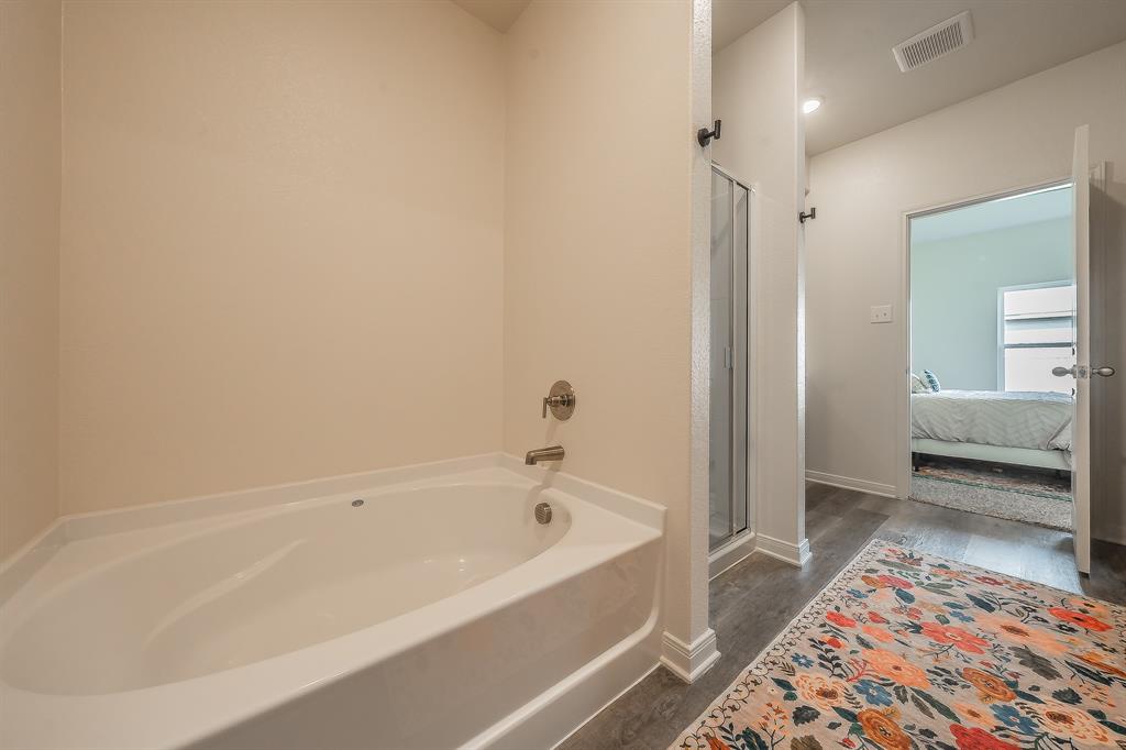 8125 White Sulphur Road Ponder, TX 76259 - Photo 16 of 38 Soaking tub with chrome fixtures, glass-enclosed shower, wood-finish flooring, and white baseboards