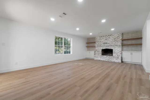 an empty room with wooden floor fireplace and windows