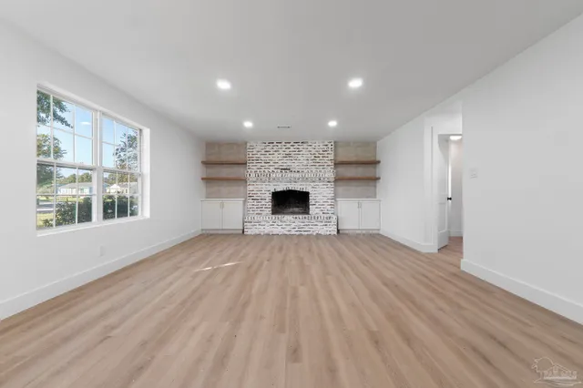 an empty room with wooden floor fireplace and windows