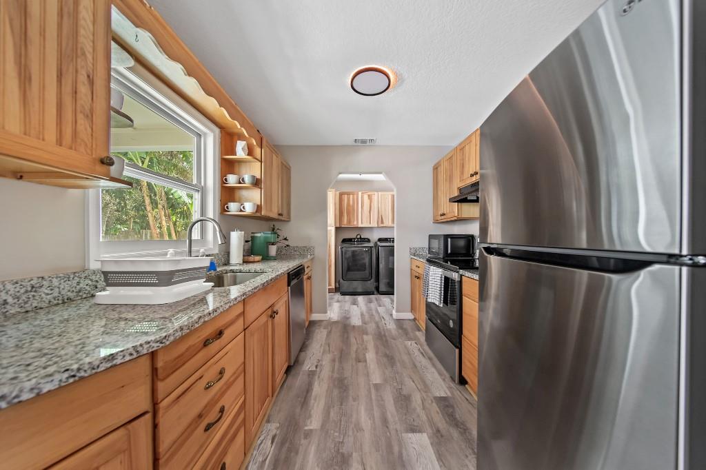 6275 Southeast Thomas Drive Stuart, FL 34997 - Photo 9 of 27 a kitchen with granite countertop a refrigerator a sink dishwasher a stove and white countertops with wooden floor