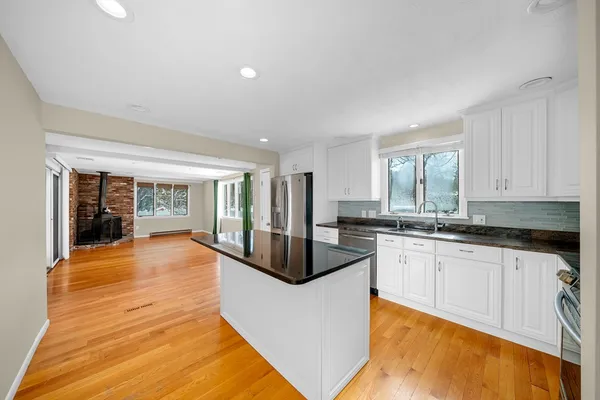 a large white kitchen with granite countertop a sink and dishwasher a stove top oven with wooden floor