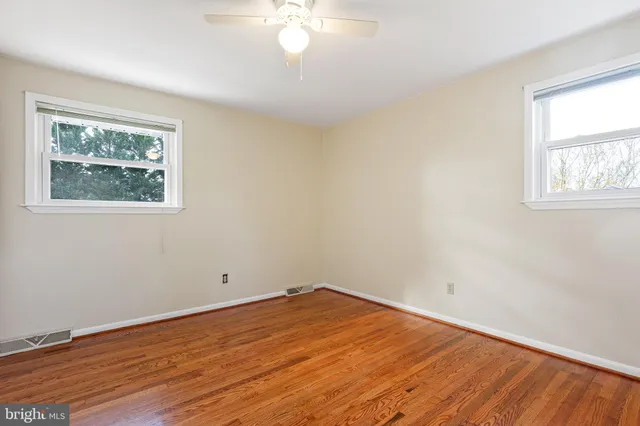 a view of empty room with wooden floor and fan