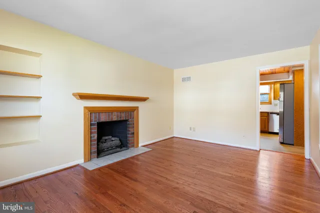 a view of an empty room with wooden floor fireplace and a window