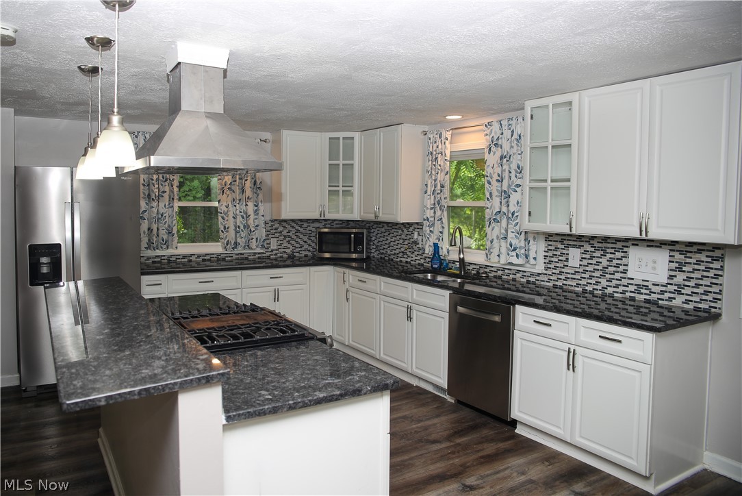 1087 Krumroy Road Akron, OH 44306 - Photo 13 of 23 Kitchen featuring a large island with cooktop, stainless steel appliances, white cabinetry, dark countertops, and a patterned tile backsplash