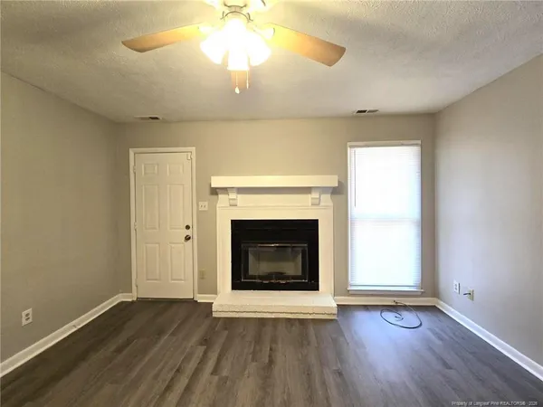 an empty room with wooden floor a chandelier fan and a fireplace