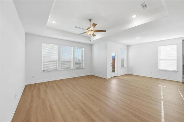 an empty room with wooden floor ceiling fan and windows