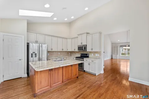 a kitchen with stainless steel appliances granite countertop a stove top oven a refrigerator a sink and dishwasher with wooden floor