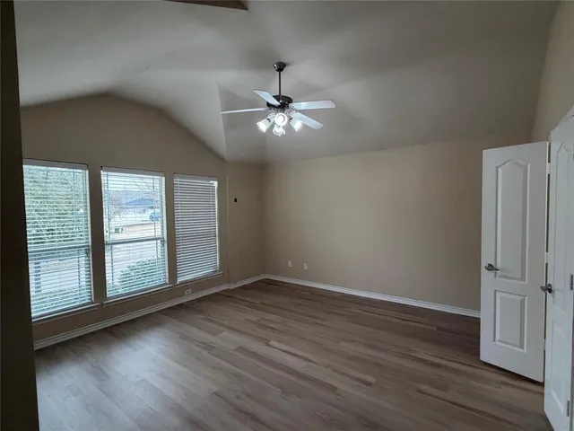 an empty room with wooden floor chandelier fan and windows