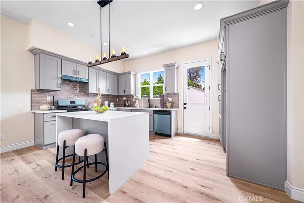 a kitchen with stainless steel appliances granite countertop a refrigerator a sink dishwasher a stove and white cabinets with wooden floor