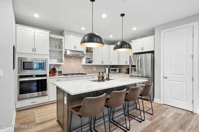 a kitchen with stainless steel appliances granite countertop a stove a sink a refrigerator a center island a stove and white cabinets with wooden floor