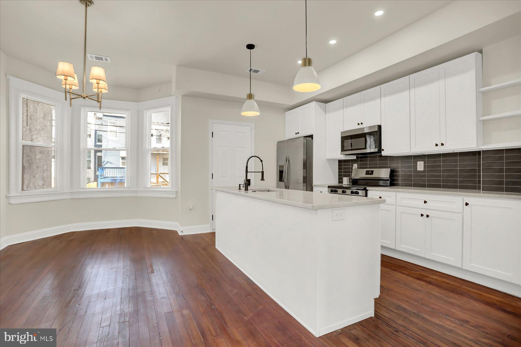 2920 Brighton Street Baltimore, MD 21216 - Photo 8 of 32 a kitchen with stainless steel appliances granite countertop a sink a microwave oven a refrigerator and white cabinets with wooden floor