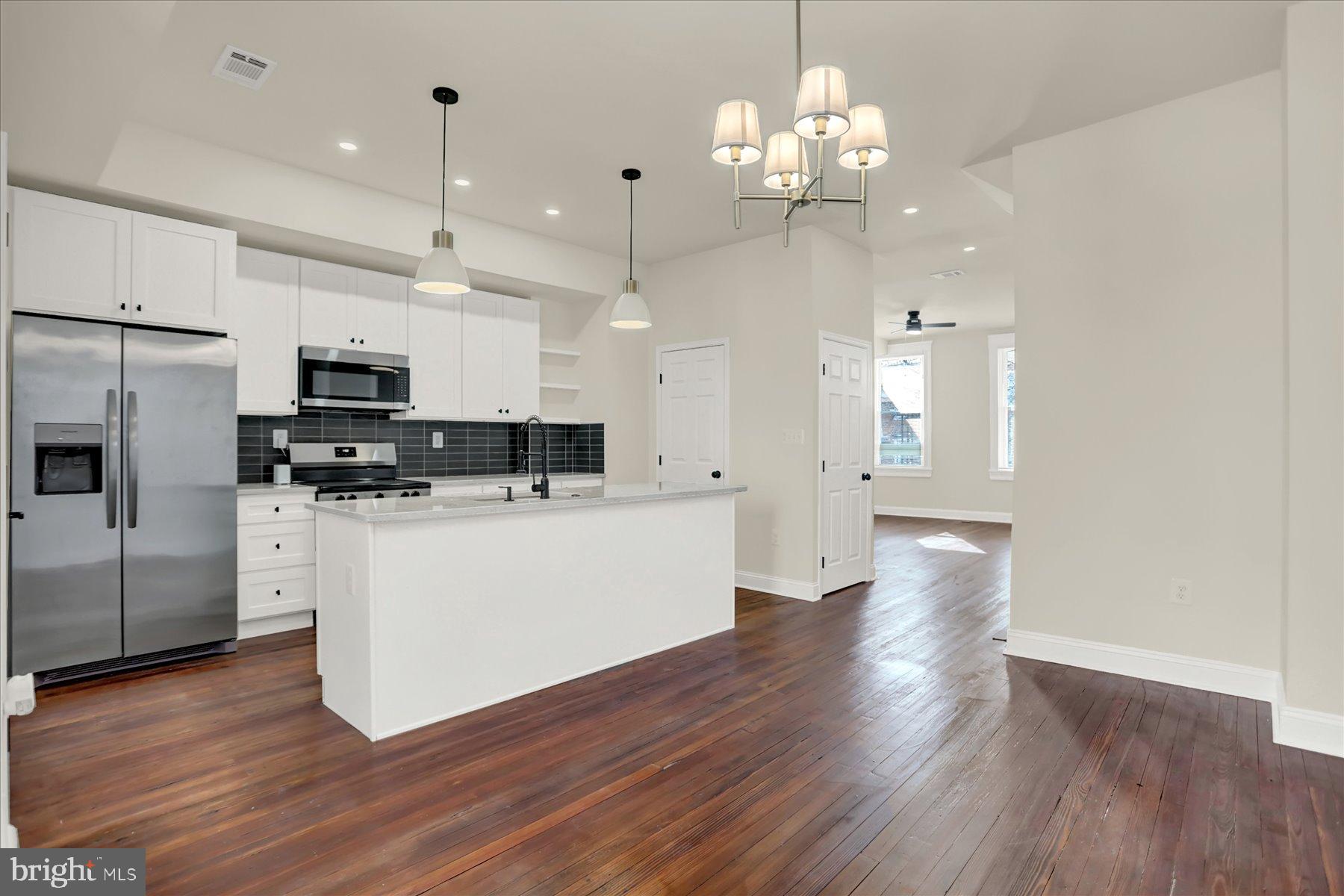 2920 Brighton Street Baltimore, MD 21216 - Photo 9 of 32 a large kitchen with granite countertop a large kitchen island a sink dishwasher a refrigerator and white cabinets with wooden floor