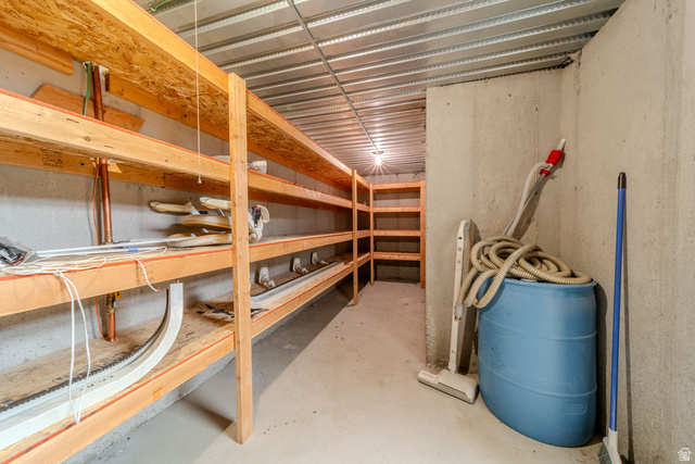 598 Hollow Creek Road Draper, UT 84020 - Photo 53 of 110 Concrete basement storage area featuring extensive built-in wooden shelving, exposed metal joists, and a concrete floor