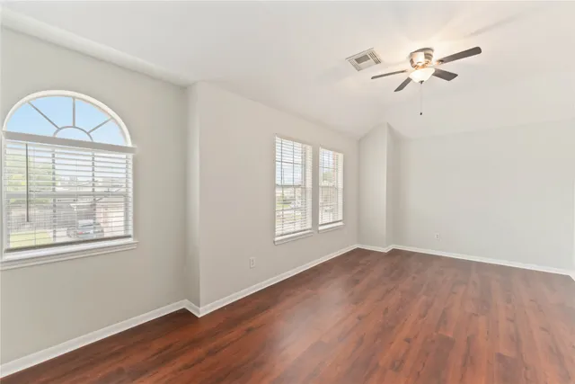 an empty room with wooden floor fan and windows