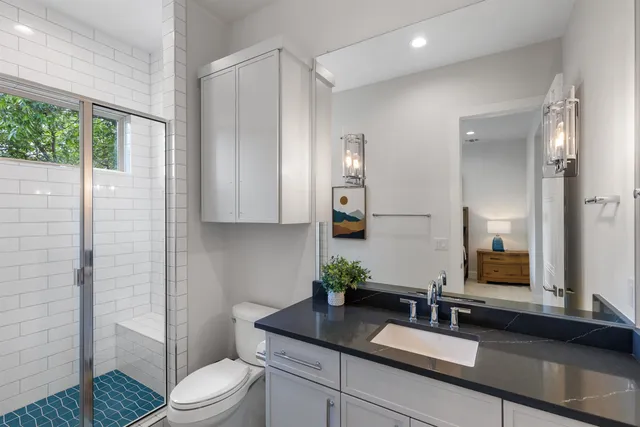 a bathroom with a granite countertop sink a toilet a mirror and shower