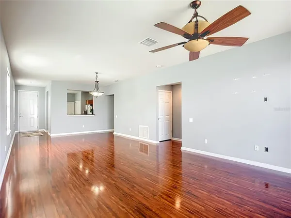 a view of an empty room with wooden floor and a ceiling fan