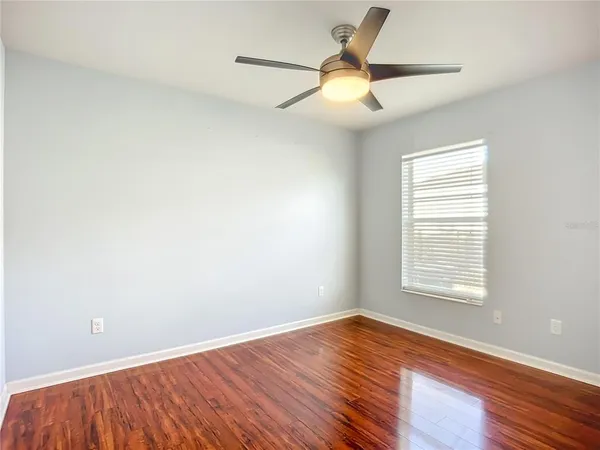 an empty room with wooden floor fan and windows
