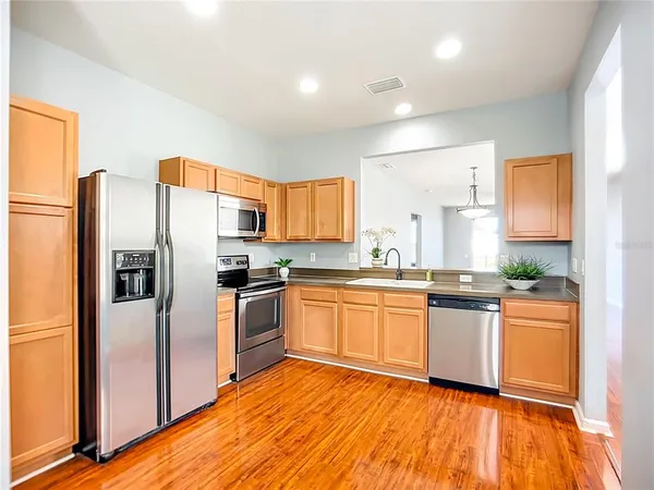 a kitchen with stainless steel appliances granite countertop a refrigerator a sink dishwasher a stove with wooden cabinets and floor