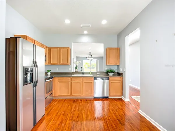 a kitchen with stainless steel appliances granite countertop a refrigerator a sink dishwasher a stove and white countertops with wooden floor
