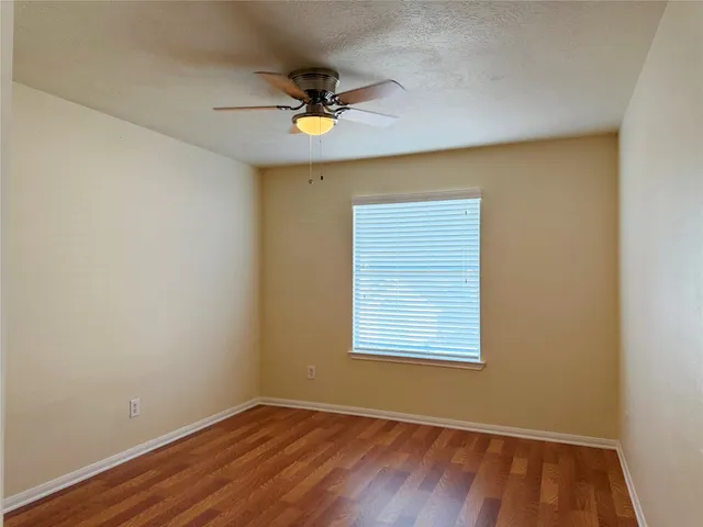 an empty room with wooden floor fan and windows
