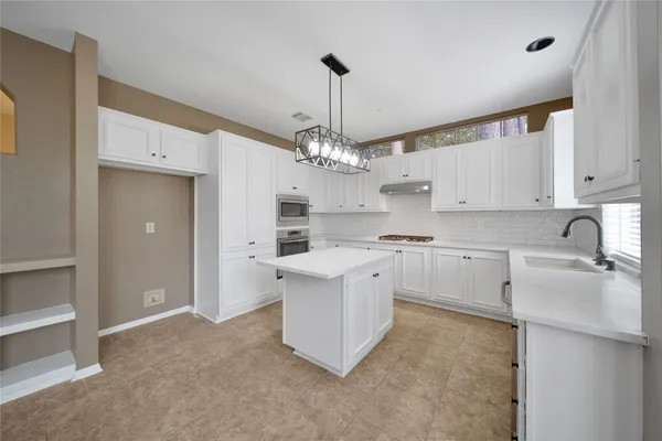 a kitchen that has a lot of white cabinets and stainless steel appliances