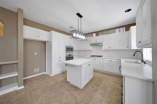 a kitchen that has a lot of white cabinets and stainless steel appliances