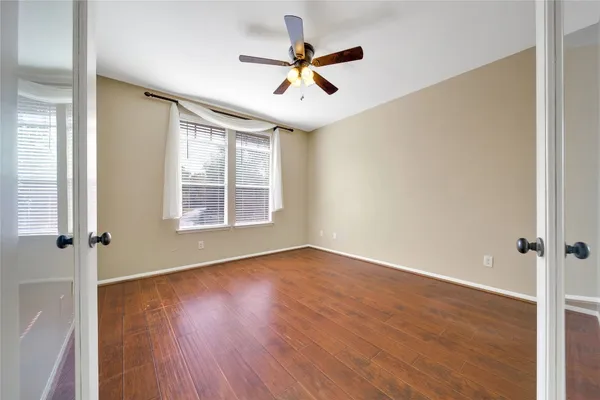 an empty room with wooden floor fan and windows