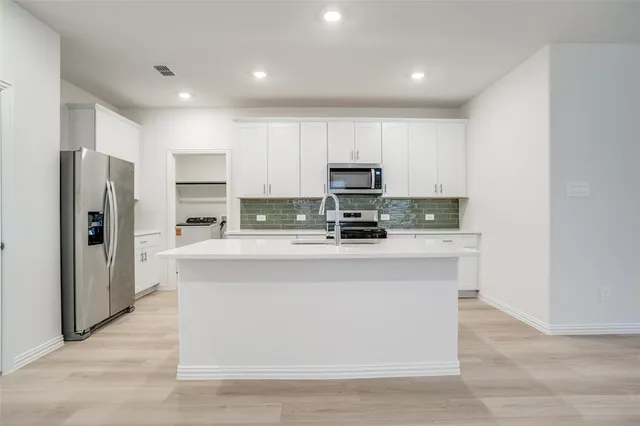 a kitchen with stainless steel appliances granite countertop a stove top oven a sink a refrigerator and white cabinets