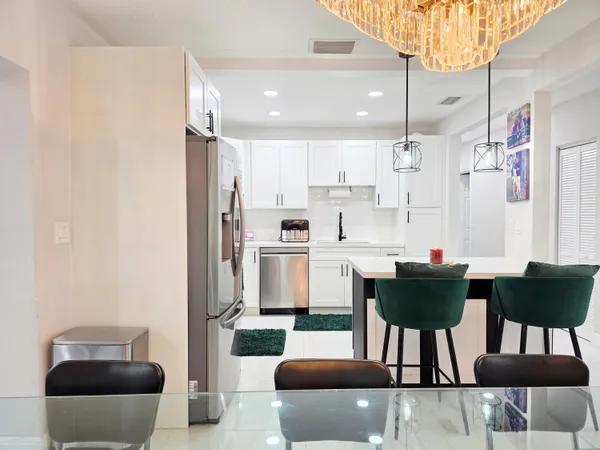 a kitchen with stainless steel appliances kitchen island granite countertop a dining table chairs and a refrigerator