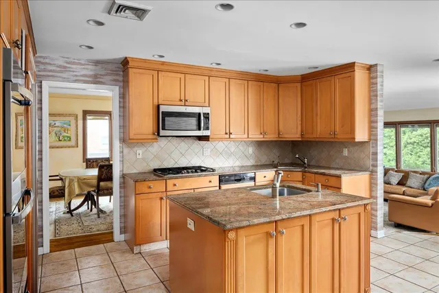 a kitchen with stainless steel appliances granite countertop a stove top oven a sink a dining table and chairs with wooden floor