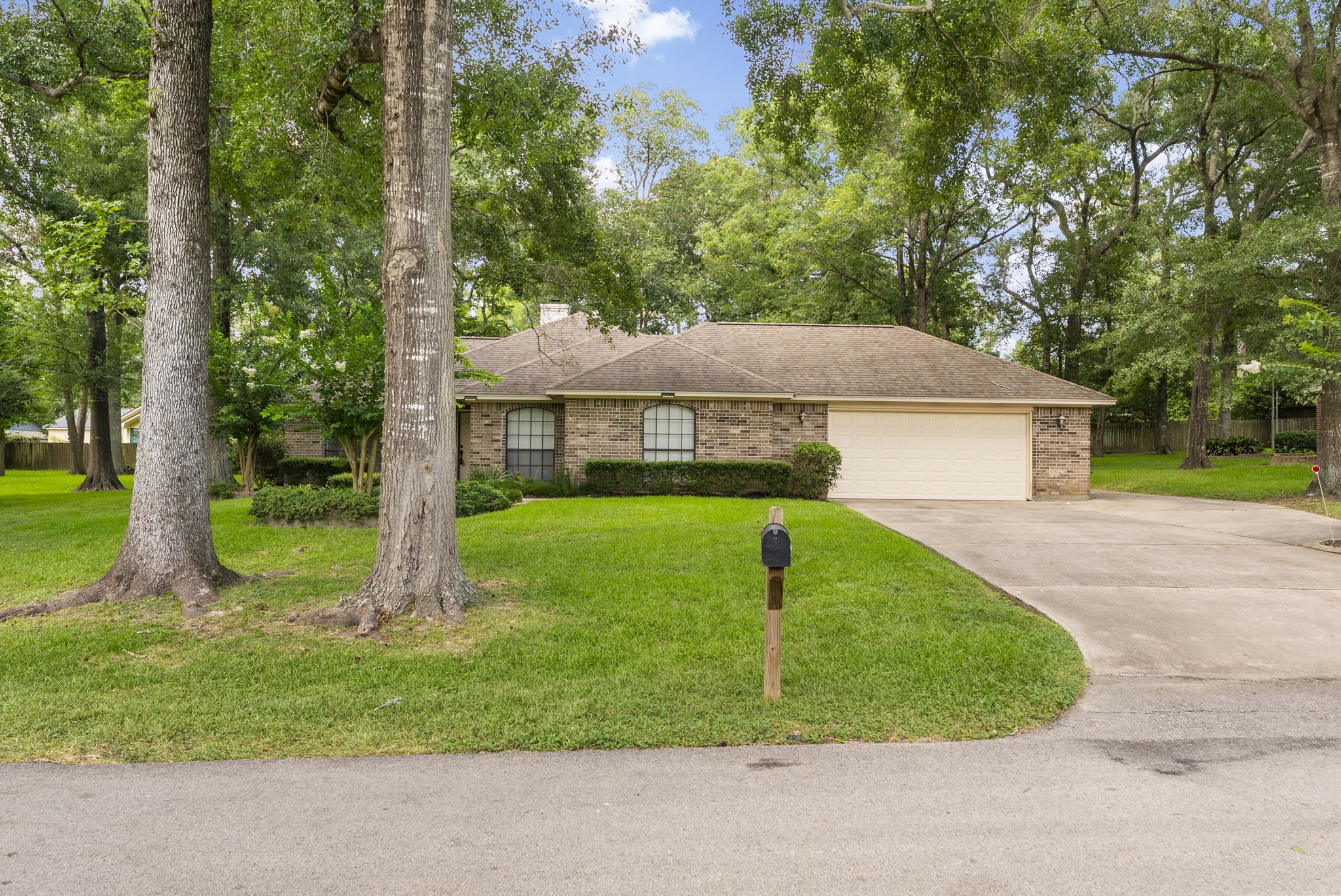 202 Sunset Boulevard Conroe, TX 77303 - Photo 3 of 50 Charming single-story brick home with a two-car garage, nestled among mature trees. Features a well-maintained lawn, a long driveway, and a tranquil suburban setting.