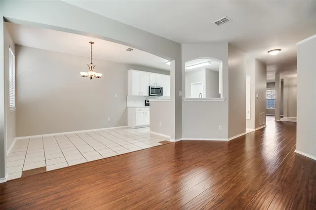 a view of an empty room with wooden floor and a kitchen