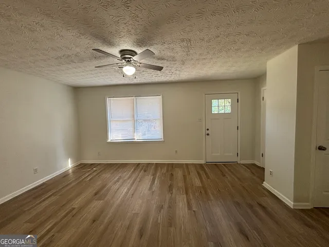 an empty room with wooden floor chandelier fan and windows