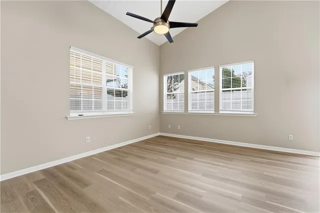 an empty room with wooden floor ceiling fan and windows