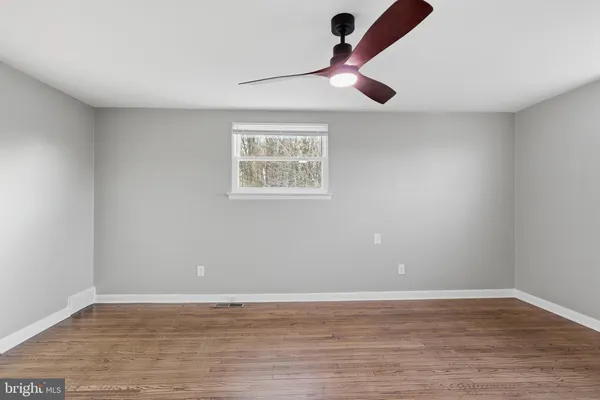 a view of an empty room with wooden floor and a ceiling fan