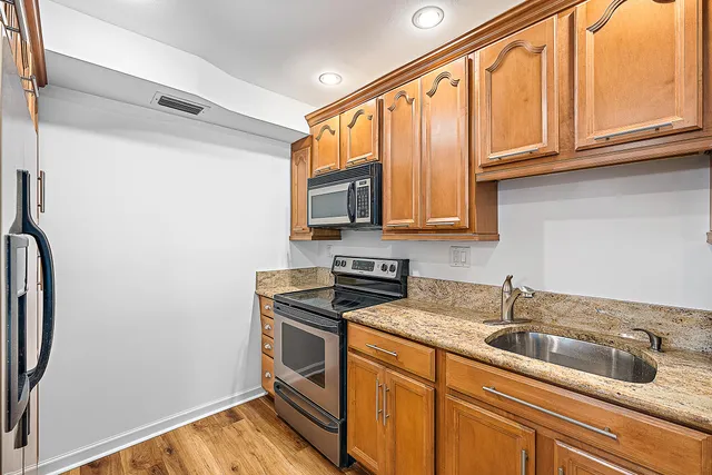 a kitchen with stainless steel appliances granite countertop a sink a stove and a refrigerator with wooden floor