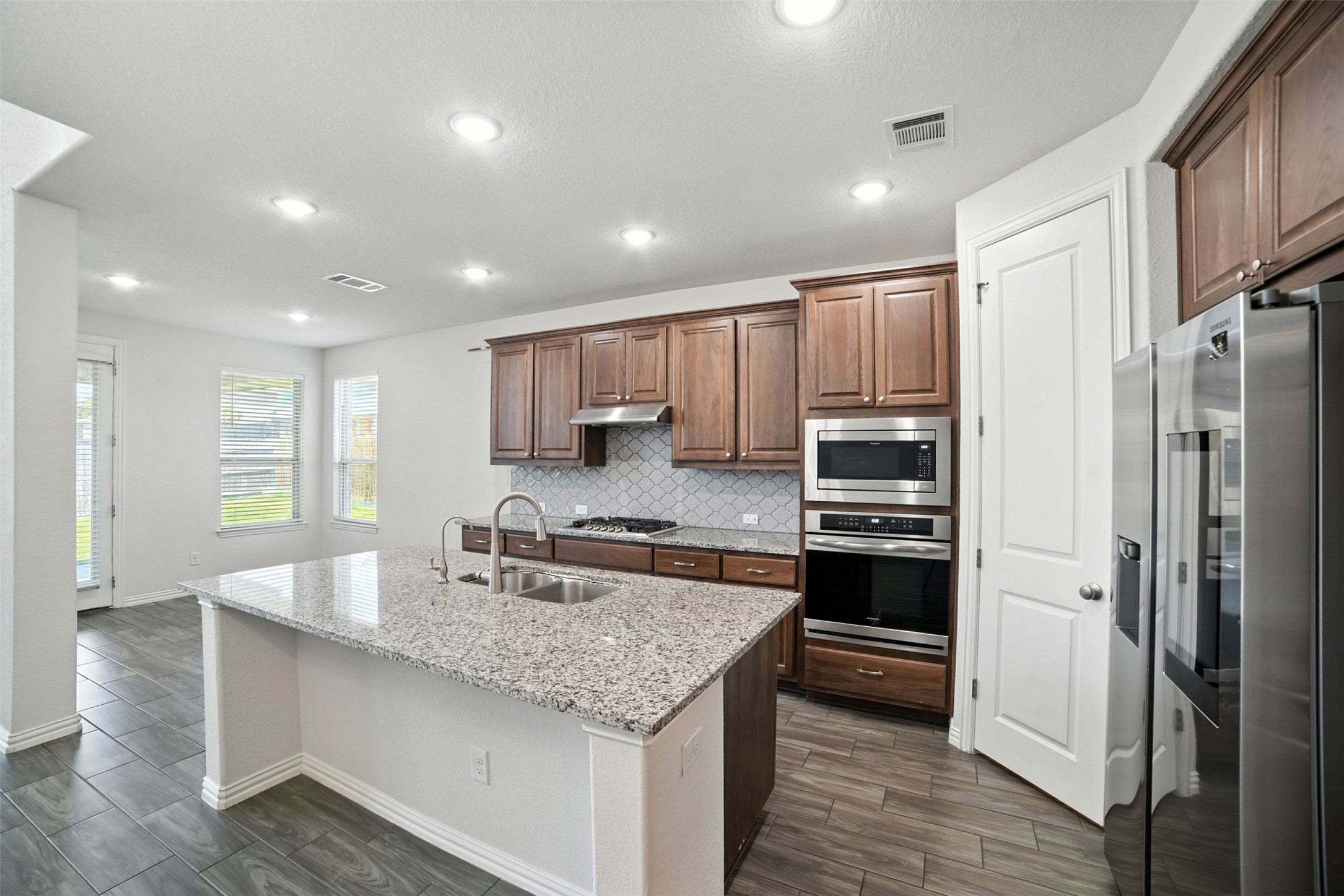 3054 Columbus Loop Round Rock, TX 78665 - Photo 8 of 40 Kitchen with stainless steel appliances, backsplash, an island with sink, light stone counters, and wood finish floors