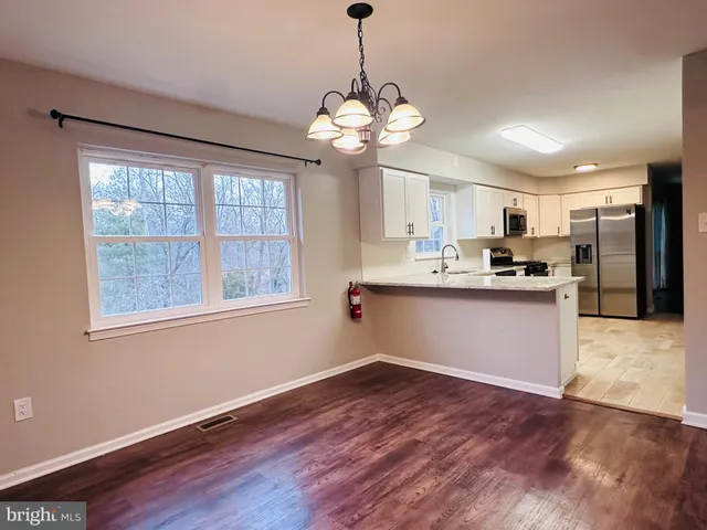 a kitchen with stainless steel appliances granite countertop a refrigerator a sink dishwasher a stove and white cabinets with wooden floor