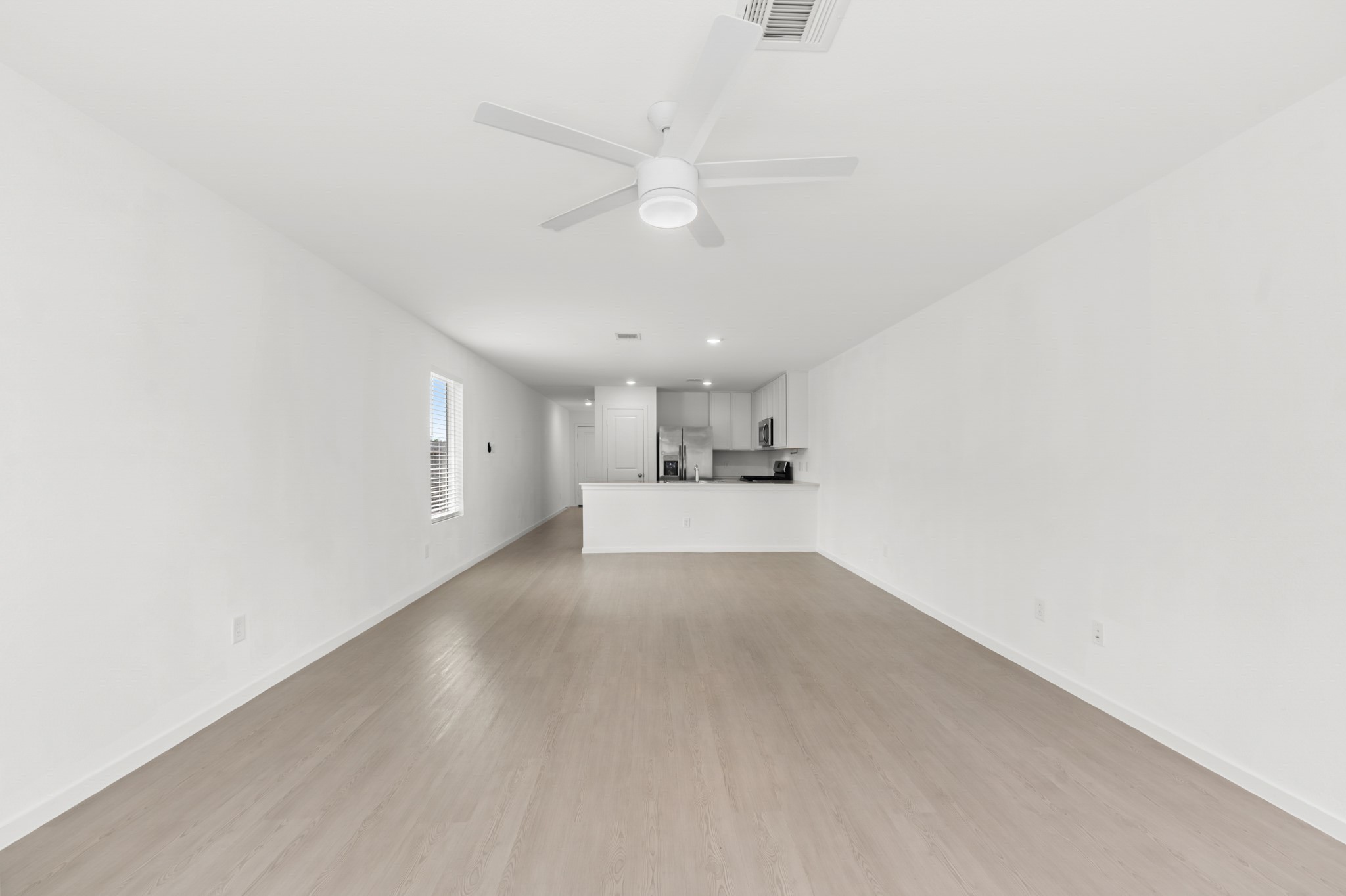 252 Houston Street Angleton, TX 77515 - Photo 15 of 49 Spacious living room offers a long, open footprint with light-toned flooring, a ceiling fan, and a direct sightline to the kitchen.