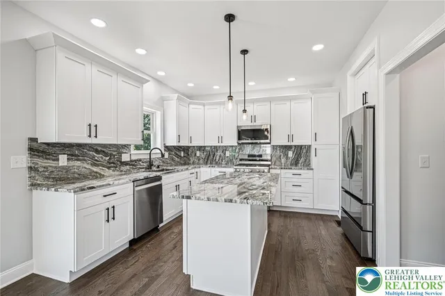 a kitchen with stainless steel appliances granite countertop a refrigerator a sink dishwasher a stove and white cabinets with wooden floor