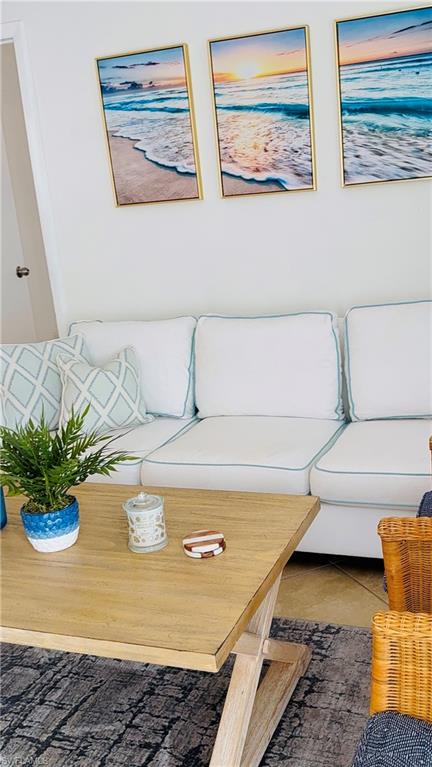 3250 10th Street North, Unit C8 Naples, FL 34103 - Photo 19 of 24 Bright living area featuring a light-toned wood-finish coffee table, white sofa with light blue piping, and a dark patterned area rug
