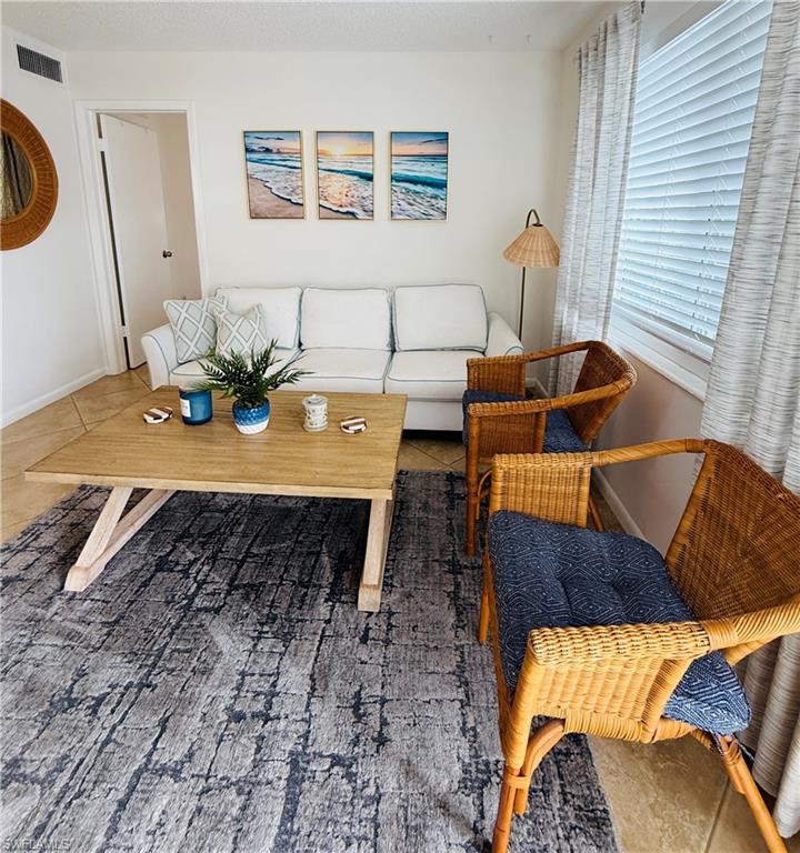 3250 10th Street North, Unit C8 Naples, FL 34103 - Photo 2 of 24 Spacious living area featuring tile flooring, a large window with horizontal blinds and drapery, and a neutral wall color