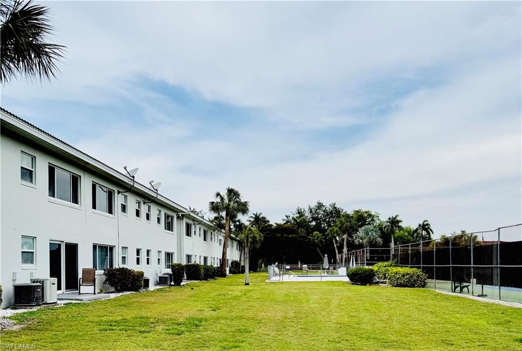3250 10th Street North, Unit C8 Naples, FL 34103 - Photo 24 of 24 Expansive lawn area featuring a tennis court with chain-link fencing, a swimming pool with surrounding deck, and multiple palm trees