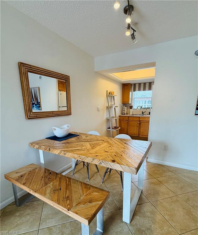 3250 10th Street North, Unit C8 Naples, FL 34103 - Photo 4 of 24 Dining area featuring tile flooring, a track lighting fixture, and a pass-through opening to the kitchen with wood cabinetry